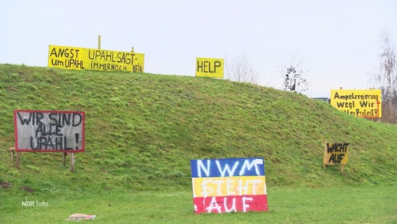 Mehrere "Protest"-Schilder gegen ein Aylbewerberheim stehen auf einer Wiese und an einem Hang. © Screenshot 