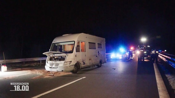 Ein Wohnmobil steht mit offener Motorhaube am Fahrbahnrand, im Hintergrund Polizeiwagen mit Blaulicht. © Screenshot 