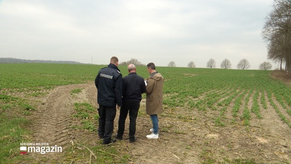 Drei Personen mit einem Bauplan auf einem Feld. © Screenshot 