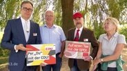 Vier Personen posieren für die Kamera. Zwei halten ein Werbeschild hoch. Auf dem einen steht "Per "Du" mit der CDU" und auf dem anderen "Auf einen Tee mit der SPD"  