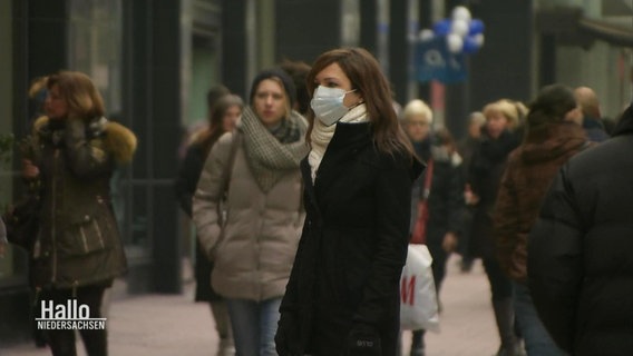 A woman with a face mask is standing in a pedestrian zone  