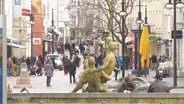 Blick auf die Innenstadt von Rostock und eine Einkaufspassage wo Menschen durchgehen. Im Vordergrund ist der Brunnen der Lebensfreude zu erkennen. 