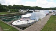 Ein kleiner Hafen an der Seenplatte, an einem Steg sind Boote in verschiedener Größe festgemacht. 