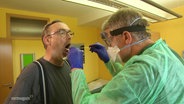 Ein Mediziner in Schutzkleidung macht einen Rachenabstrich bei einem Mann. 