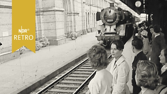 Reisende auf einem Bahnsteig bei Einfahrt eines Zuges 1960  