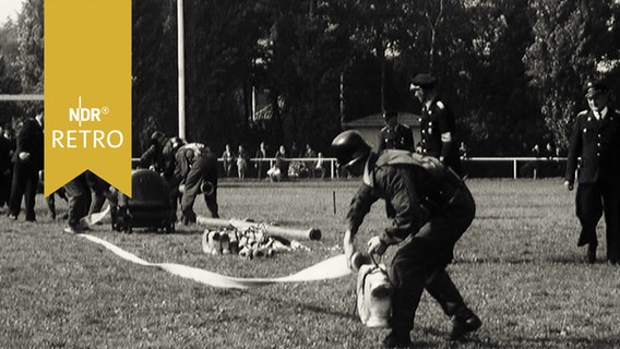 Feuerwehrleute bei einem Wettkampf beim Aufrollen eines Schlauches (1965)  