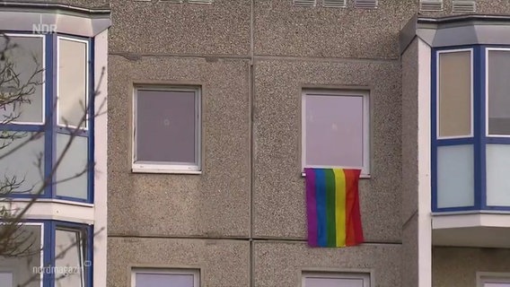 An einer Waschbeton-Fassade hängt eine Regenbogen-Flagge aus einem Fenster. © Screenshot 