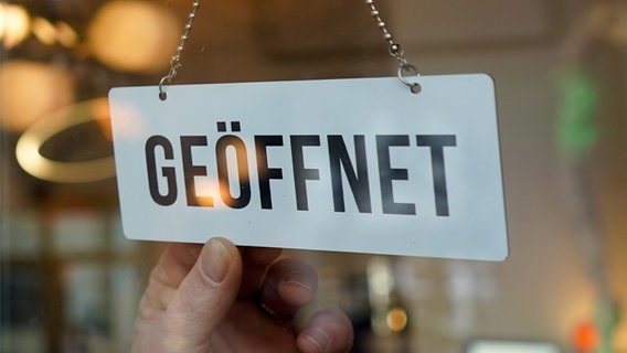 Eine Hand dreht ein Wendeschild mit der Aufschrift "Geöffnet/Geschlossen" auf "Geöffnet". (Bild: picture alliance/dpa | Jörg Carstensen) © picture alliance/dpa | Jörg Carstensen Foto: Jörg Carstensen