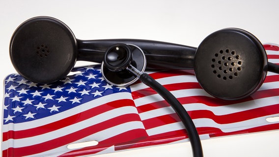 Ein Telefonhörer und ein Abhorchgerät liegen auf einer amerikanischen Flagge. © picture alliance / Roland Mühlanger Foto: Roland Mühlanger