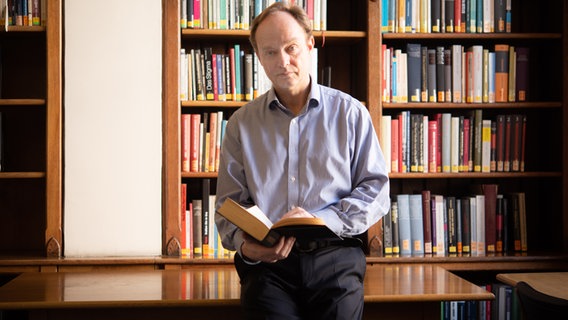 Frank Trentmann lehnt an einem Tisch und hält ein Buch in der Hand. © Jon Wilson 