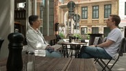 Eine Dame und ein junger Mann sitzen sich vor einem Cafe gegenüber © NDR.de 