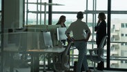 Menschen stehen vor einer Glasfassade in einem Büroraum © NDR.de 