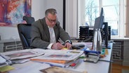 Mann sitzt am Bürotisch mit vielen Akten © NDR.de 