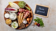 Auf einer runden Platte angeordnet sind Wurzelgemüse, Artischocke, Chicoree, Zwiebel, Knoblauch, Kefir, Kräuterquark, Kimchi und Gewürze. Daneben eine Tafel: "Darmgesund" © NDR Foto: Claudia Timmann