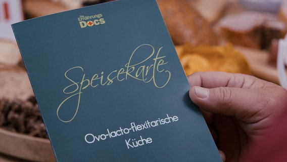 Hand hält eine Speisekarte mit der Aufschrift "ovo-lacto-flexitarische Küche". © NDR Foto: Oliver Zydek  Moritz Schwarz