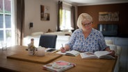 Eine blonde Frau sitzt am Esstisch und blättert in Kochbüchern. © NDR Foto: Moritz Schwarz/Oliver Zydek