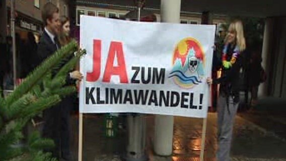 Tobi Schlegl rollt ein Plakat mit der Aufschrift "Ja zum Klimawandel" aus. © NDR Foto: Screenshot