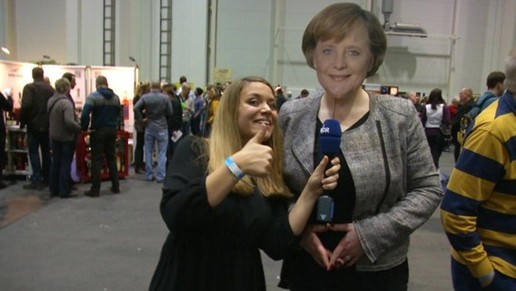 Die NDR-Reporterin Jasmin Al-Safi steht neben einer Angela Merkel Pappfigur.  