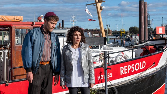 Eine Frau und ein Mann stehen vor einem Schiff, das im Hafen liegt. © ARD/Thorsten Jander 