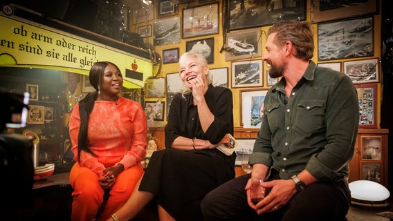 Motsi Mabuse, Ina Müller und Klaas Heufer-Umlauf sitzen bei Inas Nacht auf dem Tresen. © NDR/ Morris Mac Matzen Foto: Morris Mac Matzen