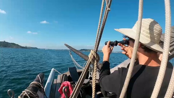 Eine Frau mit Strohhut schaut mit Hilfe eines Fernrohrs auf einem Schiff in die Ferne © NDR.de 