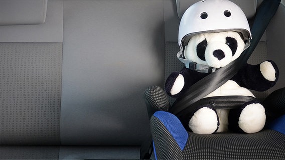 Ein Stofftier mit Helm ist auf einem Rücksitz im Auto angeschnallt. © fotolia Foto: S.Kobold