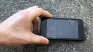 Hand hält defektes Smartphone vor steinigem Boden. © fotolia Foto: ronstik