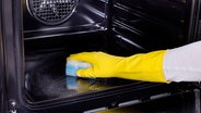 Eine Hand mit gelbem Gummihandschuh und Putzschwamm in einem Backofen. © Fotolia.com Foto: Budimir Jevtic