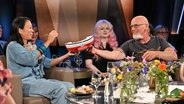 Björn Both, Frontmann der Band Santiano, reicht der Schauspielerin Minh-Khai Phan-Thi in der NDR Talk Show ein Spenden-Schiffchen der DGzRS hinüber und sie wirft eine Münze ein. © NDR Fernsehen/ Uwe Ernst Foto: Uwe Ernst