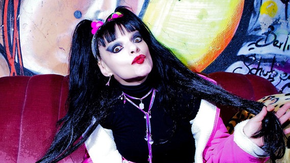 Sängerin Nina Hagen mit schwarzen langen Haaren, die zu zwei Zöpfen gebunden sind. Sie macht große Augen und zeigt einen roten Kussmund. © Mey/polydor Foto: Mey/polydor