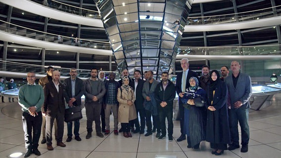 Die Kollegiaten des Islamkolleg stellen sich mit dem Abgeordneten Mathias Middelberg (CDU, im Anzug mit Krawatte) zu einem Foto unter der Kuppel des Bundestags auf. © NDR 