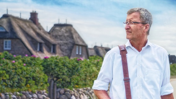 Montage: Straße in Rantum auf Sylt. Burkhard Jansen in Oberhemd und mit Brille blickt zur Seite. © NDR/Philipp Nöhr | Look: Ulla Brauer Foto: Philipp Nöhr