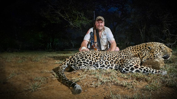 Nachtaufnahme - Carlo Engelhardt hockt lächelnd mit Gewehr im Arm hinter einem erschossenen Leoparden. © Carlo Engelhardt Foto: Carlo Engelhardt