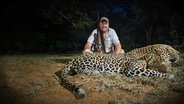 Nachtaufnahme - Carlo Engelhardt hockt lächelnd mit Gewehr im Arm hinter einem erschossenen Leoparden. © Carlo Engelhardt Foto: Carlo Engelhardt