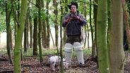 Szenenbild aus der 90. Büttenwarder-Folge "Trüffel": Shorty steht mit einem Schwein im Wald. © NDR/Nico Maack Foto: Nico Maack