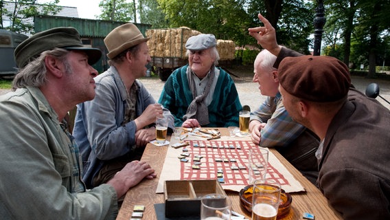 Szenenbild aus der 37. Büttenwarder-Folge "Vizekönig": Brakelmann, Adsche, Onkel Krischan, Shorty und Kuno sitzen vorm Dorfkrug am Tisch. © NDR/Nicolas Maack 