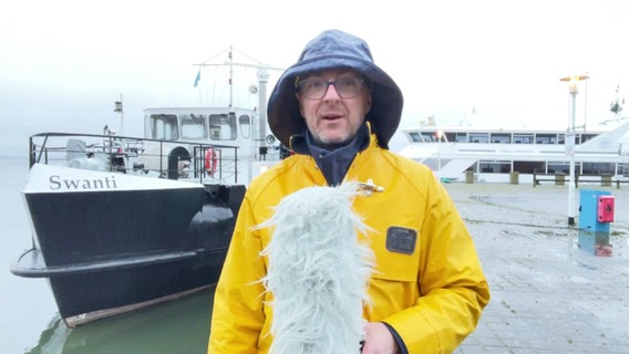 Stefan Kreibohm steht in Regenkleidung am Hafen der Insel Hiddensee und präsentiert das Wetter. © Screenshot 