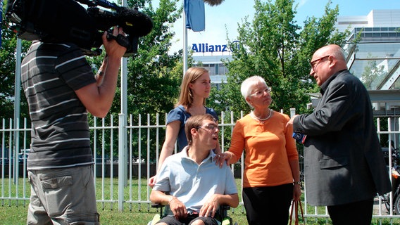 Christoph Lütgert mit Versicherungsopfern vor einem Gebäude der Allianz. © NDR 