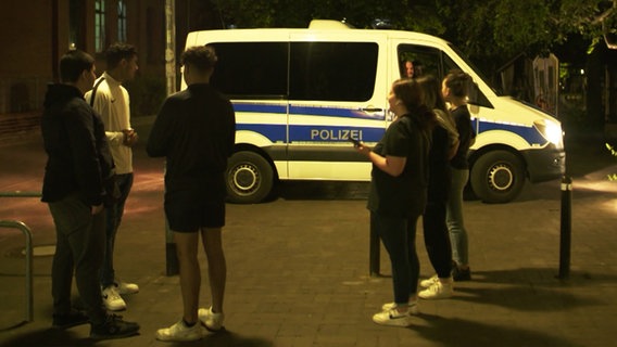 Polizisten stehen vor mit einem Einsatzwagen neben einer Gruppe Jugendlicher. © NDR Foto: Screenshot