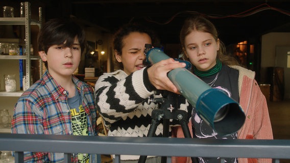 Jules, Taara und Malin beobachten das Nachbarhaus mit dem Fernrohr. © NDR/Letterbox 