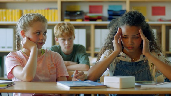 Malin (Ida Carlo) sorgt sich um Taara (Josefine Maxima), die schon wieder Kopfschmerzen hat, genau wie Noah (Gero Drews) hinter ihnen. © NDR/Letterbox 