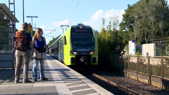 An einem Bahnsteig stehen ein Frau und ein Mann während ein Zug einfährt. © NDR 