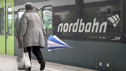 Eine Frau mit Regenschirm geht an einem Zug der nordbahn entlang, der im Bahnhof steht. © picture alliance/Bodo Marks Foto: Bodo Marks