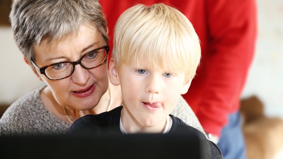 Eine ältere Frau hat einen Jungen auf dem Schoß und gemeinsam blicken sie auf einen Laptopbildschirm. © NDR Foto: Berit Ladewig