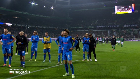 Spieler von Holstein Kiel und ihr Trainer Marcel Rapp stehen auf dem Fußballfeld bei Werder Bremen. © NDR 