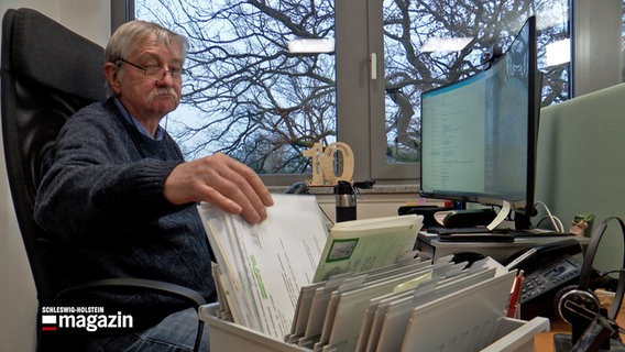 Ein äterer Mann sitzt in seinem Büro an seinem Arbeitstisch. © NDR 