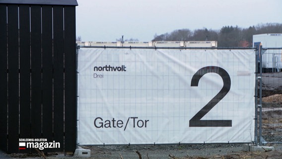 Ein weißer Banner mit dem Schriftzug Northvolt drei Tor/Gate 2 hängt an einem Baustellenzaun bei Heide. © NDR 