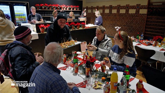 Menschen sitzen an einem Tisch beim Weihnachtsessen für Obdachlose in der Stadtmission Kiel. © NDR 