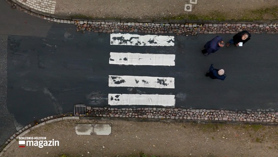 Drei Männer stehen auf einer Straße in Ratzeburg unweit eines Zebrastreifens. © NDR 