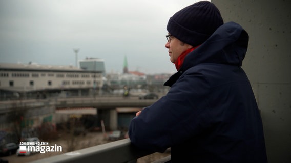 Ein Mann mit einer Brille und einer Mütze steht auf einer Brücke in Kiel. © NDR 